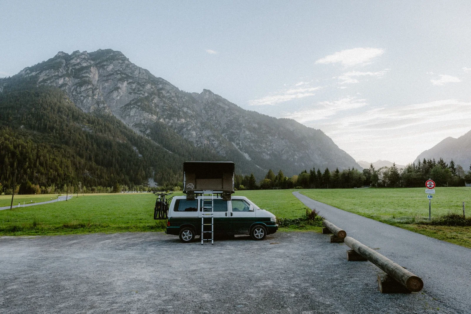 VW Camper mit Dachzelt an einem befestigten Weg vor Bergkulisse