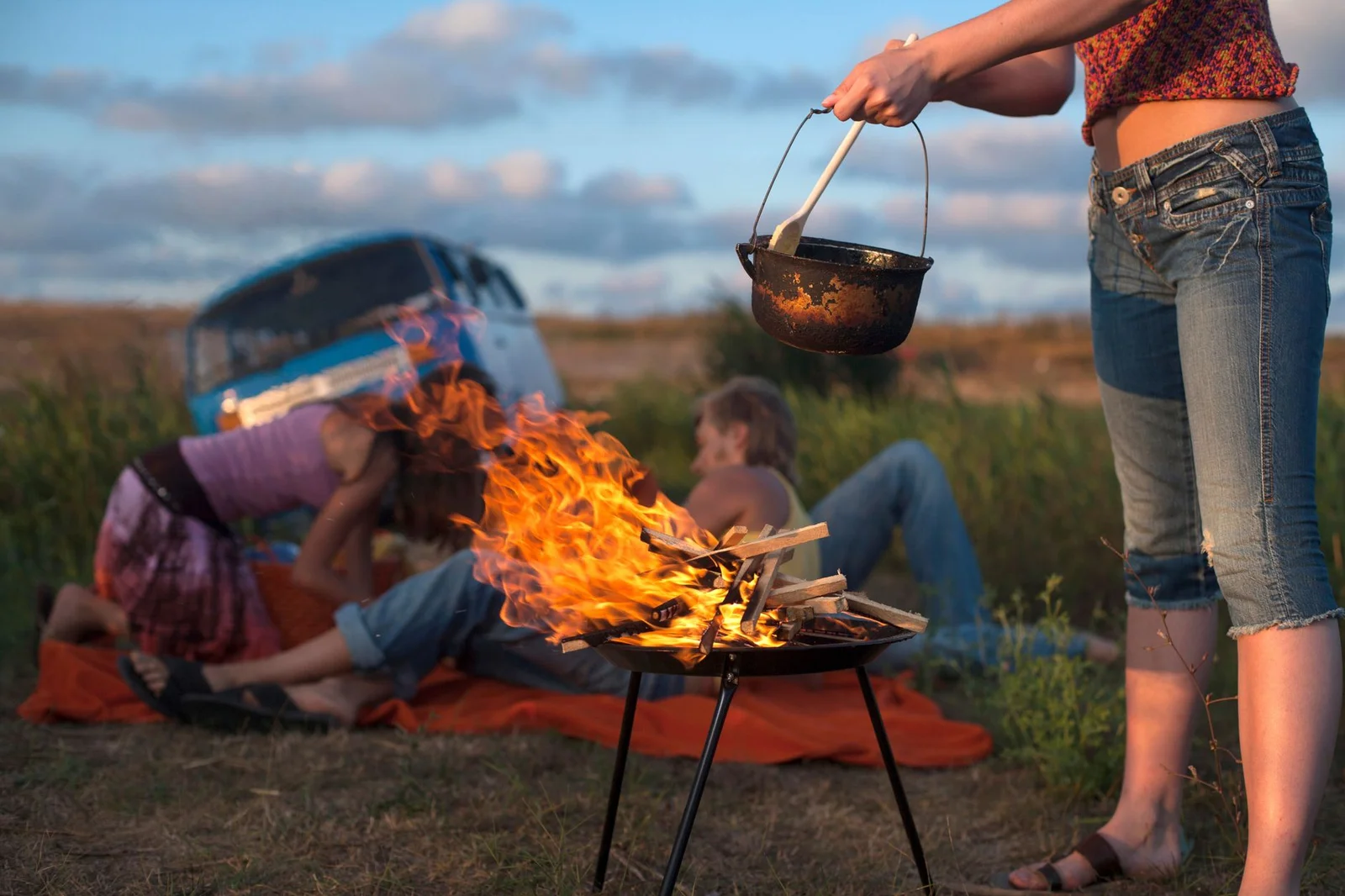 Gruppe kocht gemeinsam am Lagerfeuer neben einem Camper-Van auf dem Stellplatz