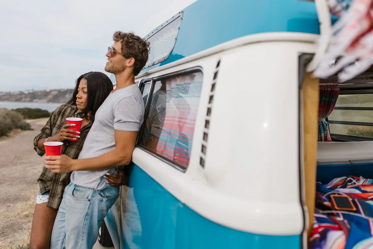 Paar neben einem Campervan mit geöffneter Tür und sichtbarem Gepäck