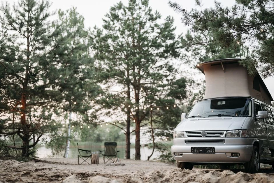 Campervan mit Aufstelldach an einem bewaldeten Seeufer