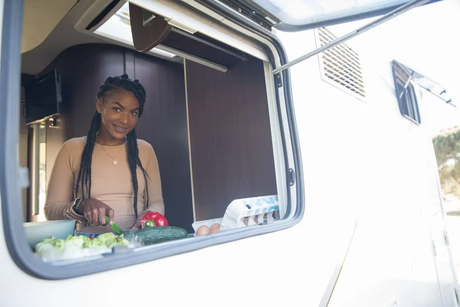 Frau lehnt sich aus dem Fenster eines Campers und bereitet Gemüse für das Kochen vor