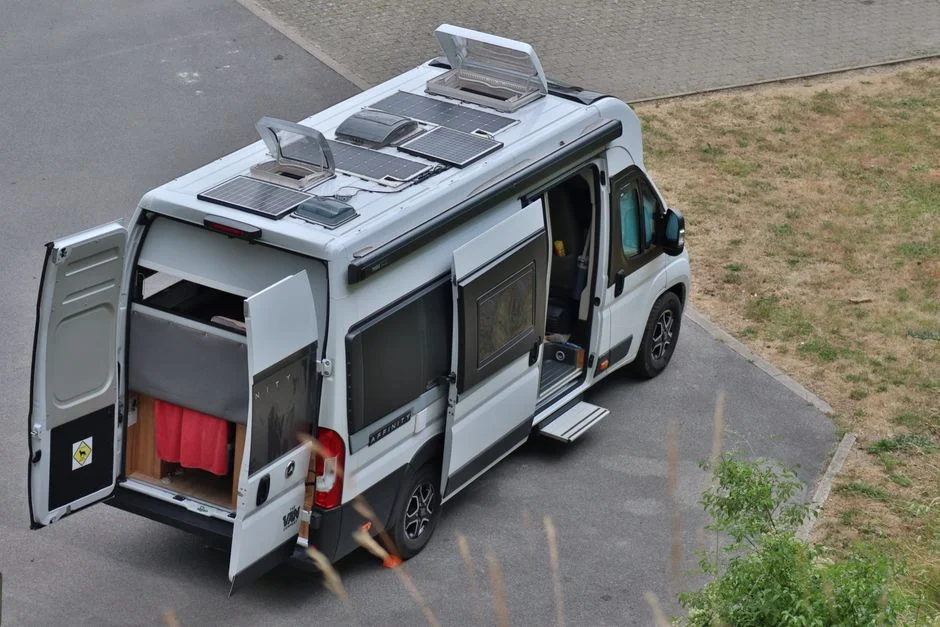 Camper Van mit geöffneten Hecktüren, offener Schiebetür und Solarmodulen auf dem Dach