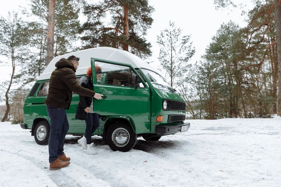 Grüner Campervan auf einer verschneiten Waldzufahrt bei Tageslicht