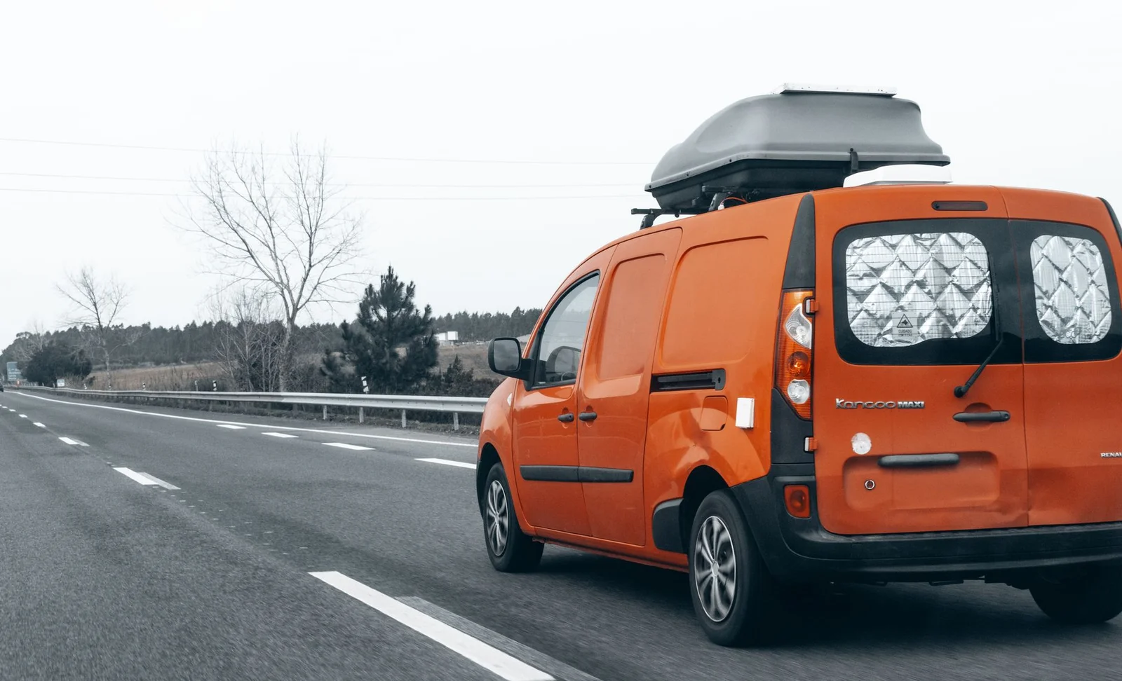 Oranger Van mit Dachbox auf einer hellen Autobahnfahrt