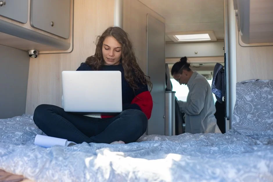 Frau mit Laptop auf der Liegefläche in einem hellen Camper-Innenraum