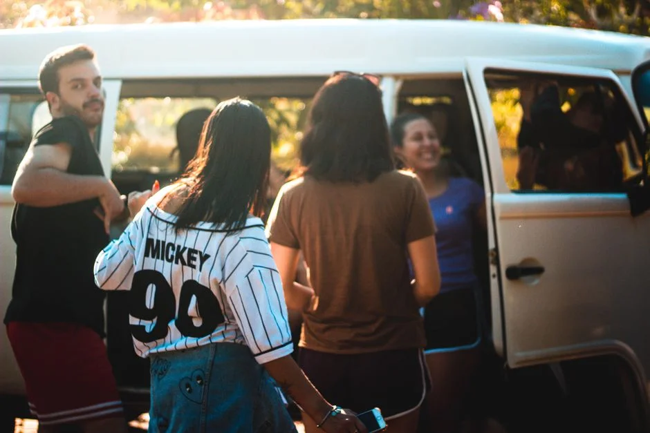 Gruppe junger Leute an der geöffneten Schiebetür eines VW Bus im Abendlicht