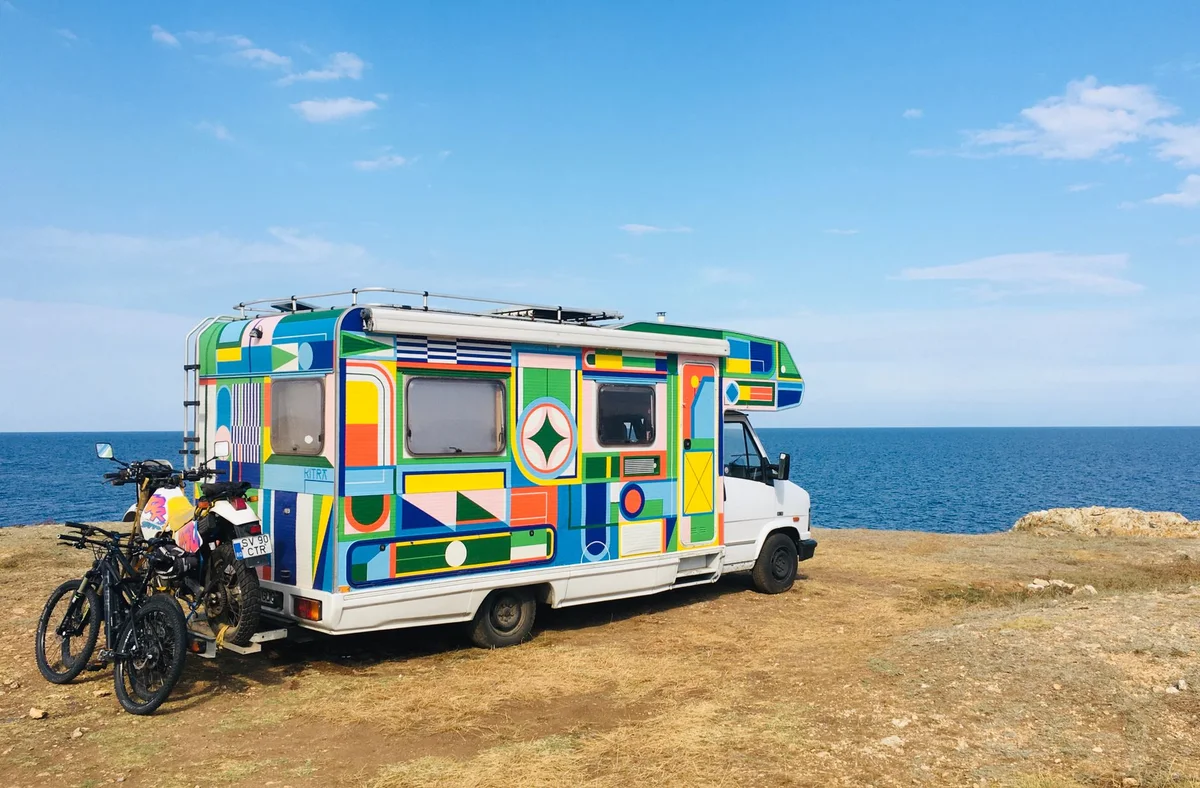 Bunter Campervan mit zwei Fahrrädern auf einem Heckträger am Meer