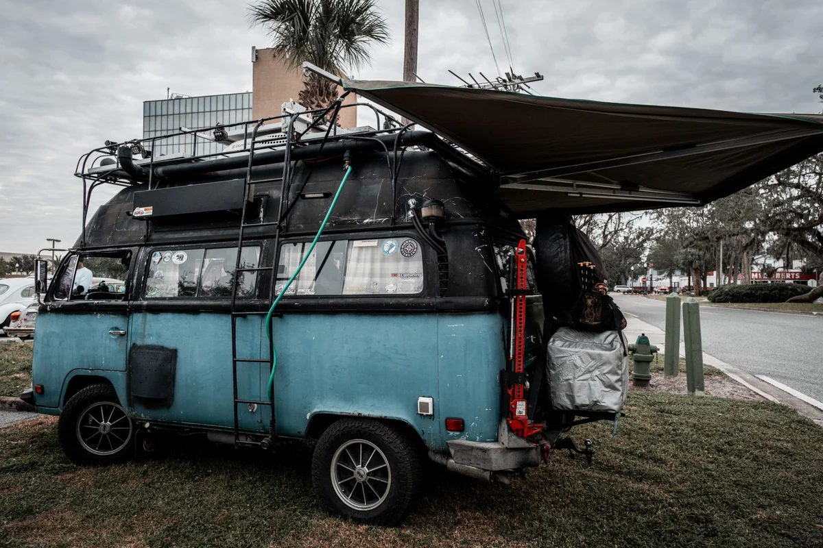 Blauer Volkswagen Camper mit ausgefahrener Markise und Reiseausrüstung