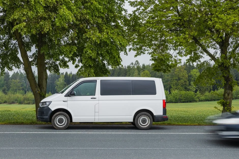 Weißer VW Transporter am Straßenrand vor grünen Bäumen bei Tageslicht