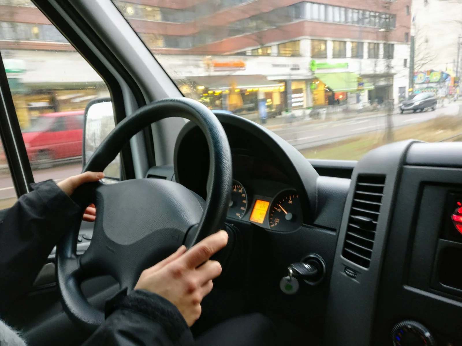 Hände am Lenkrad eines Vans beim Fahren durch eine Stadt bei Tageslicht