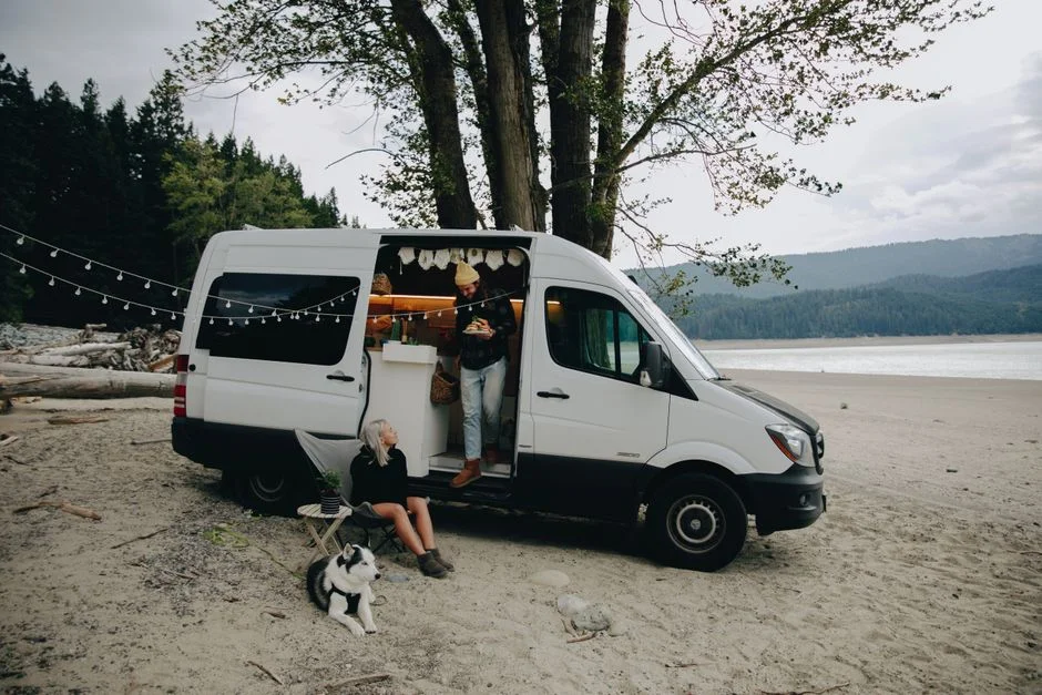 Camperbus mit geöffneter Schiebetür auf einem Stellplatz am Wasser