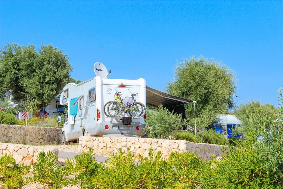 Wohnmobil mit ausgefahrener Markise und Fahrrädern am Heck auf einem sonnigen Campingplatz